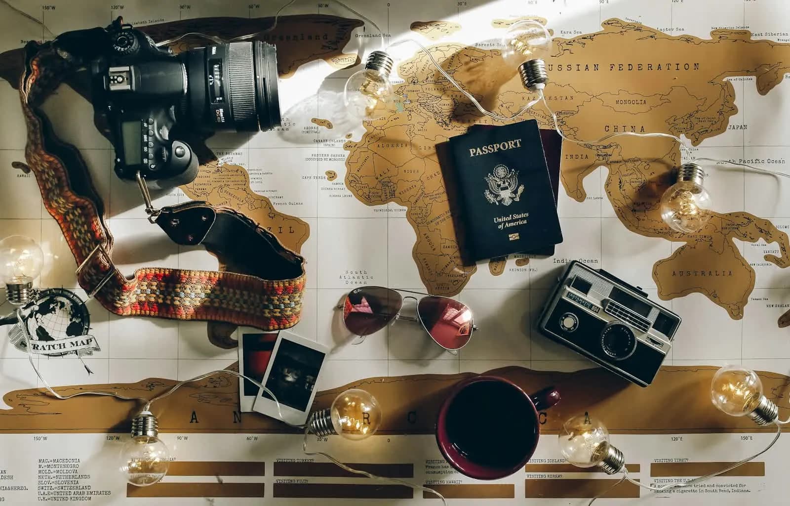 A world map covered with a passport, cameras, sunglasses and photos while a trip is planned