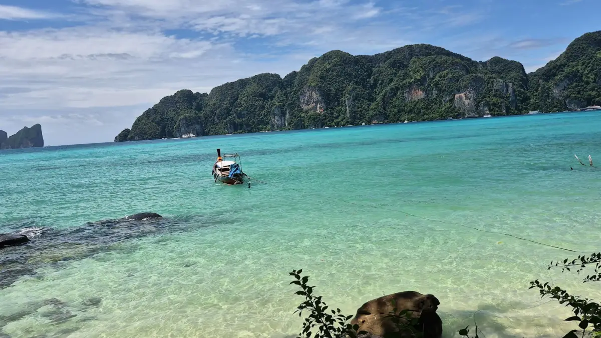 Long-tail boat floating in clear turquoise water near limestone cliffs in Thailand